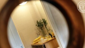 Ein Badezimmer mit einem Spiegel, der ein Waschbecken, eine Pflanze und einen Handtuchhalter reflektiert.