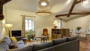 Ein geräumiges Wohnzimmer mit einer großen grauen Couch, einem Holzregal, einer Essecke mit Tisch und Stühlen sowie einer Pendelleuchte.