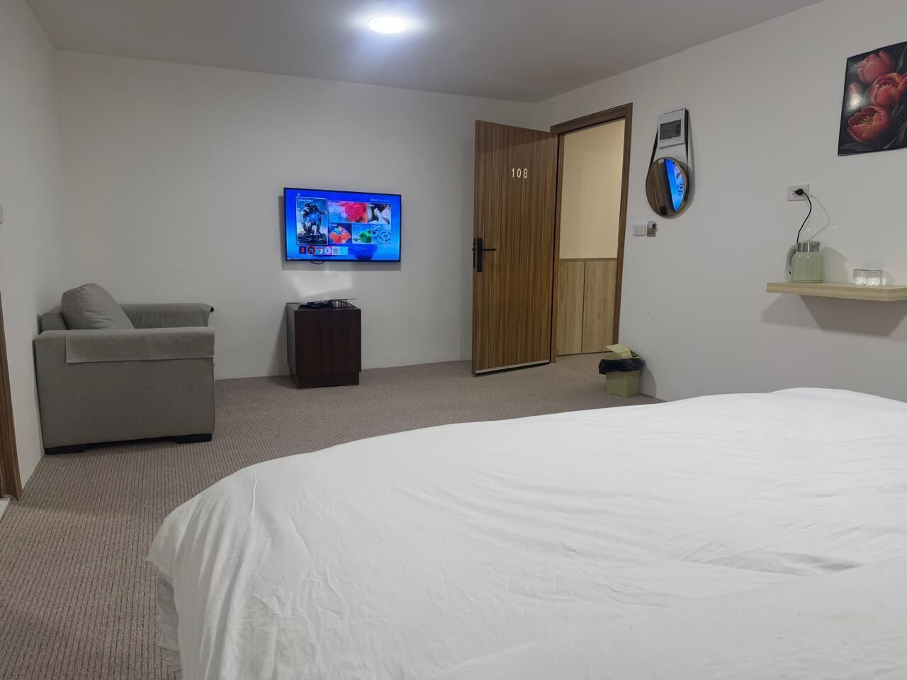 Habitación de hotel con una cama grande, televisión, armario de madera y un pequeño rincón de descanso.