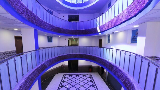 A multi-level hotel lobby with a central atrium, glass railings, and a checkered floor pattern. - Skylight Apartments (Amman)