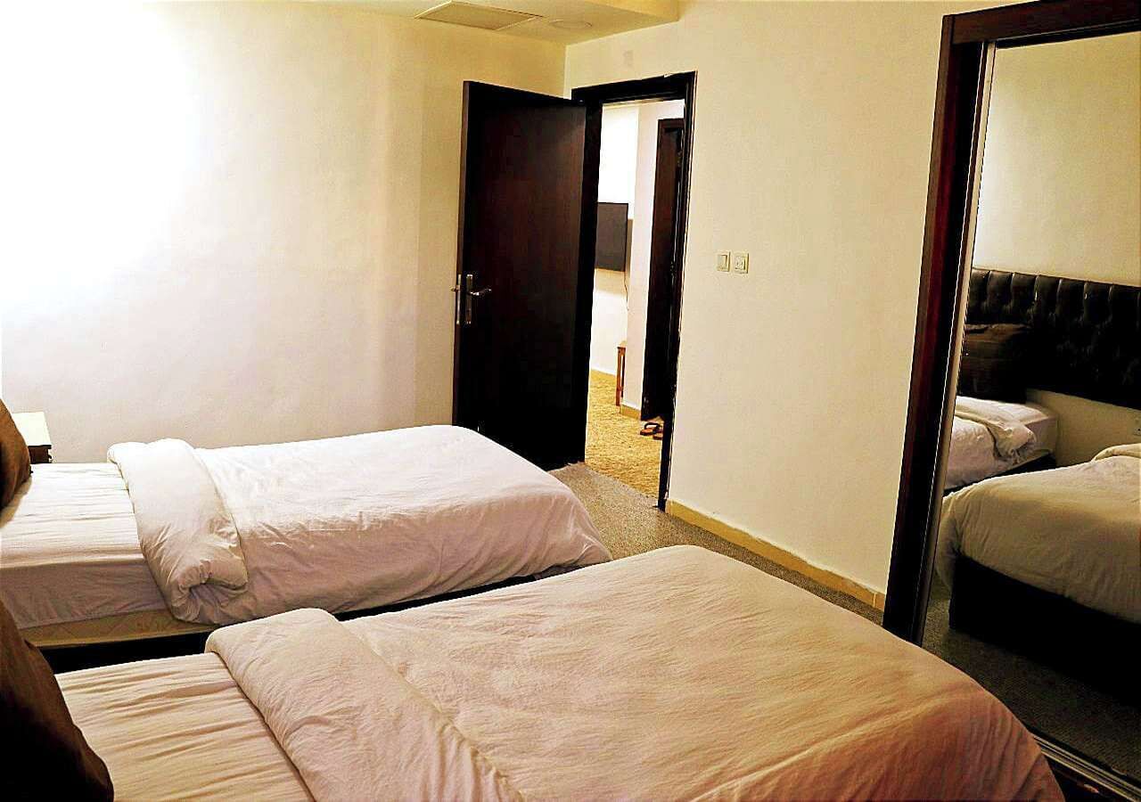A hotel room with two single beds, a large mirror, and a door leading to a hallway.