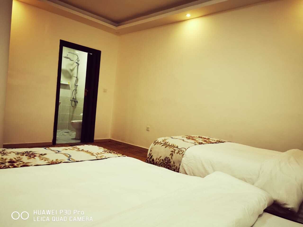 Habitación de hotel con dos camas, zona de ducha y pared lisa.