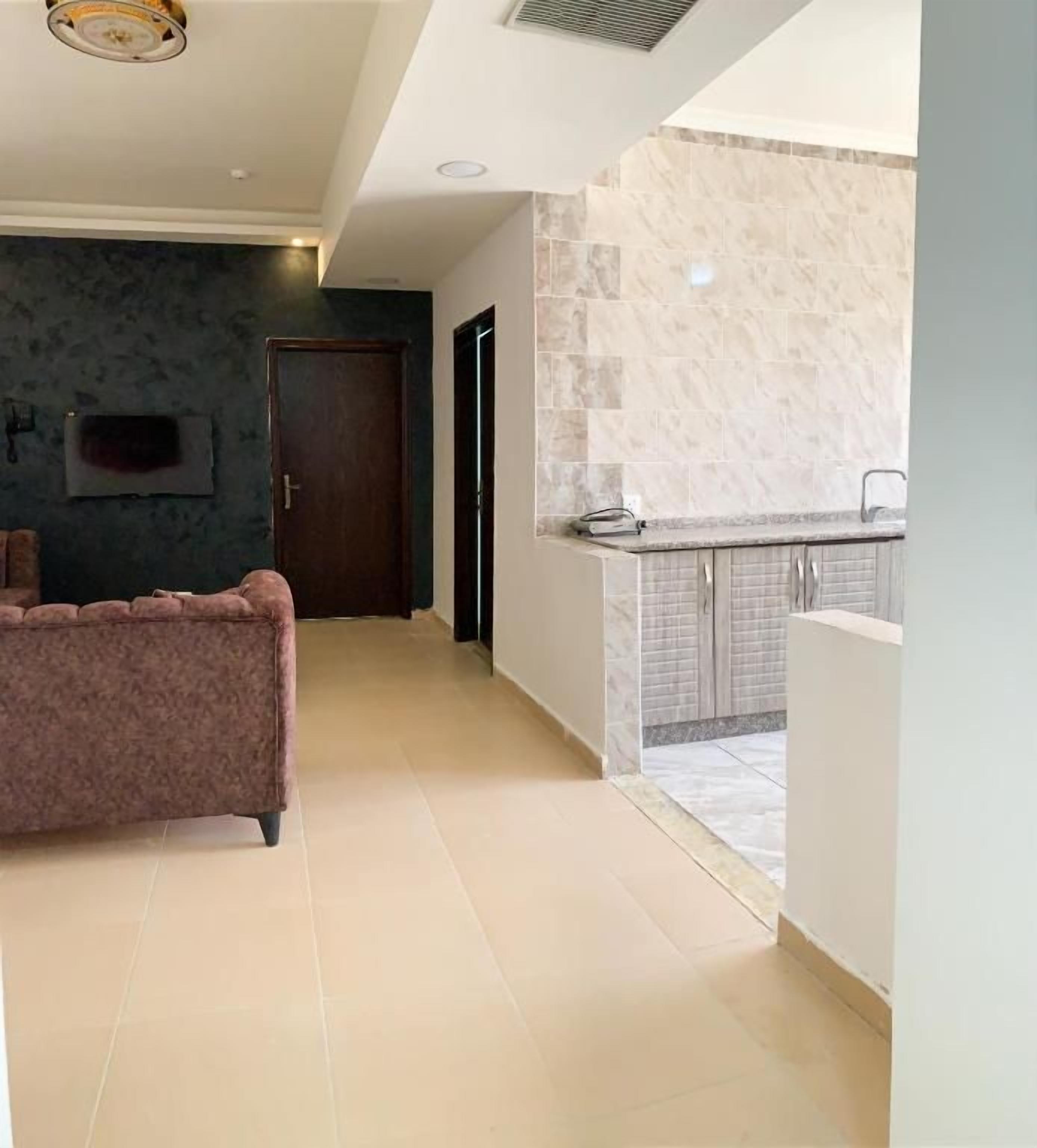 Un interior moderno con un sofá, una zona de cocina con salpicadero de mármol y una puerta que da a otra habitación.