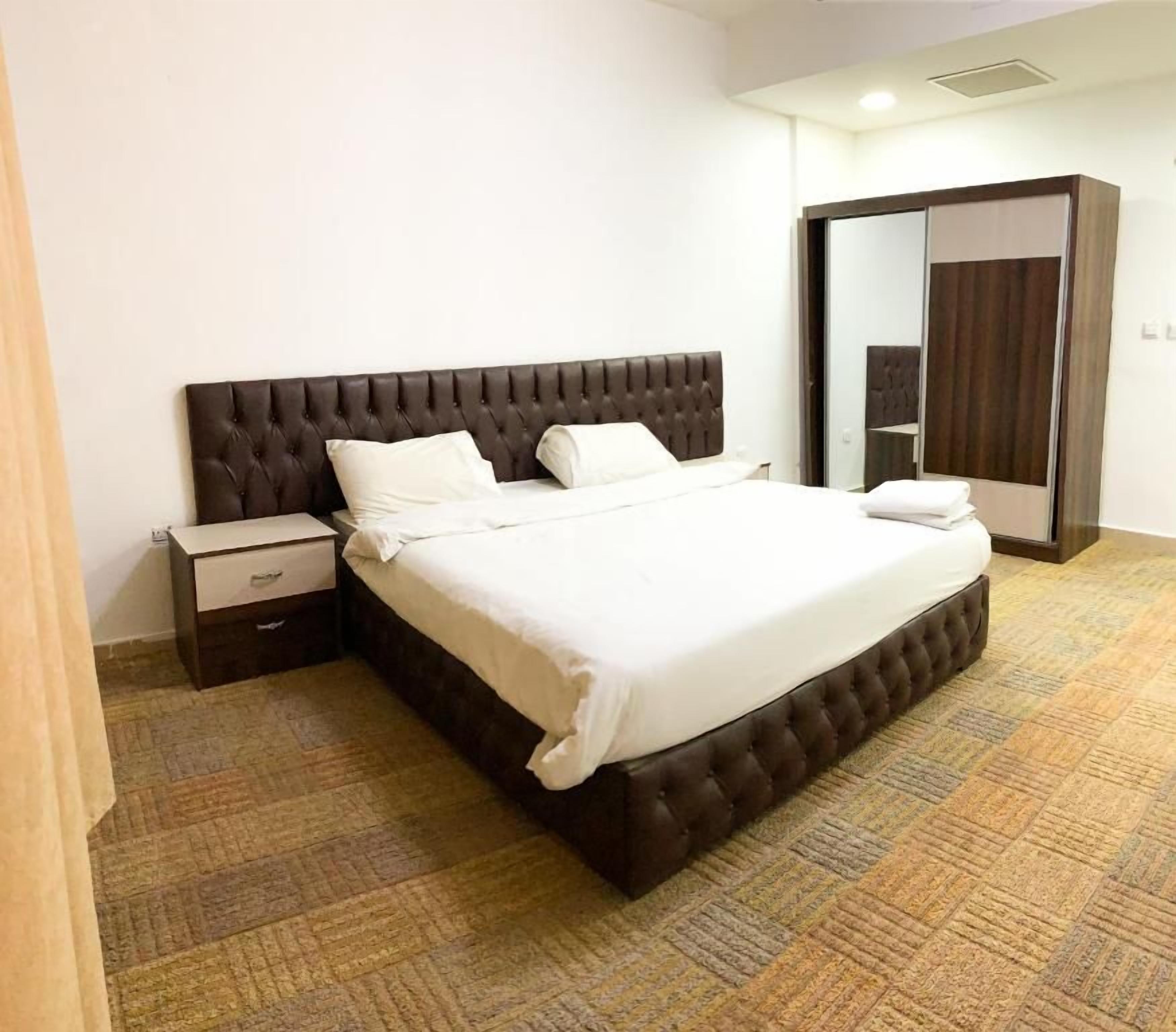 Ein Hotelzimmer mit einem großen Bett, einem Nachttisch, einem Kleiderschrank und Teppichboden.