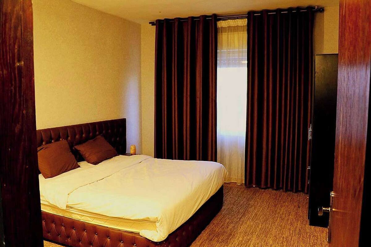 Una habitación de hotel con una cama grande, cortinas oscuras y una puerta de madera.