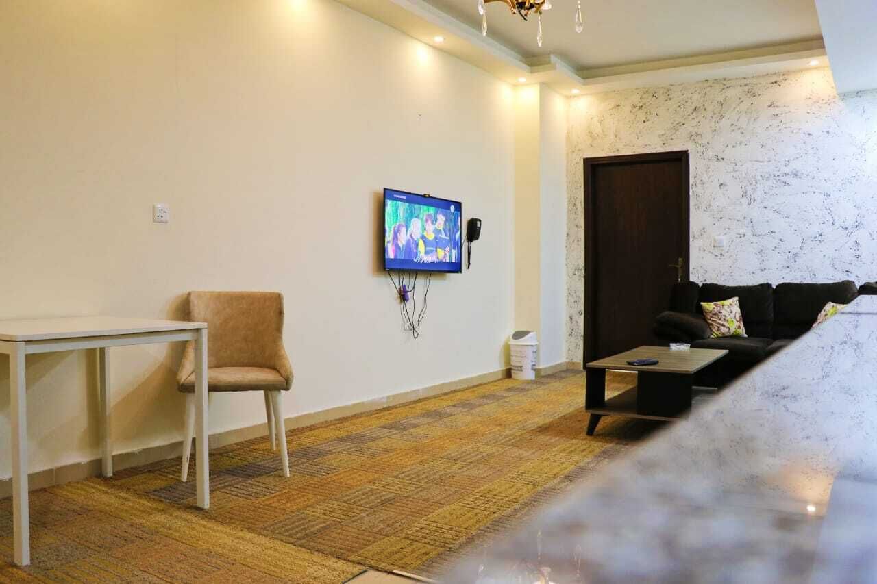 A living room with a television mounted on the wall, a sofa, a small table, and a chair.