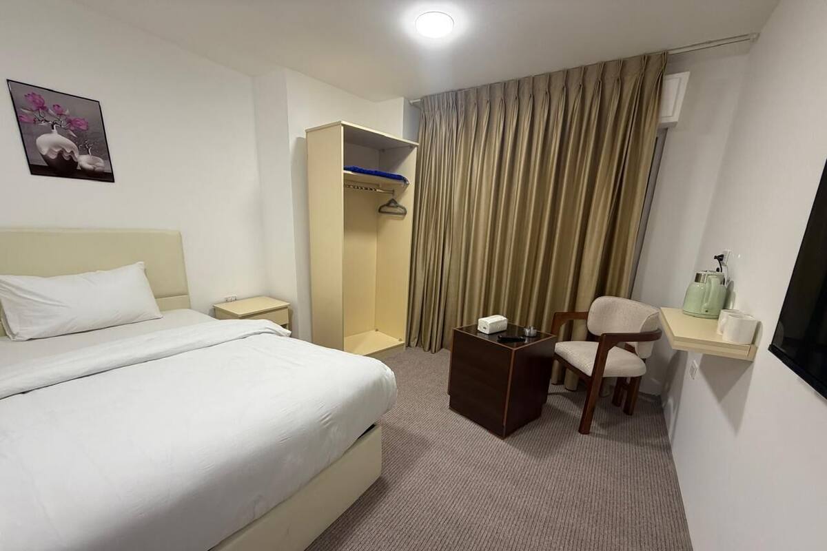 Una habitación de hotel con cama, escritorio, silla, armario y cortina.