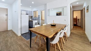 Eine moderne Küche mit weißen Schränken, einer Mikrowelle und einem Fenster. Ein Essbereich mit Holztisch und weißen Stühlen ist ebenfalls vorhanden.
