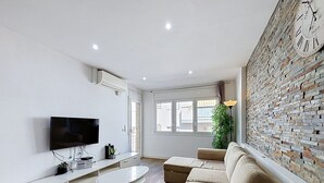 Ein modernes Wohnzimmer mit Flachbildfernseher, einem weißen Sofa, einem runden Couchtisch und einer Wand mit Ziegeloptik.