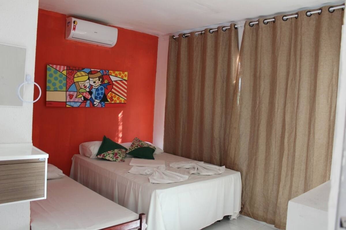A room with two beds, a colorful painting on the wall, an air conditioning unit, and a curtain.