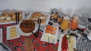 A table with various food items and drinks, including bread, pastries, sliced fruits, and a cake. - Encantos dos Sonhos (Ipojuca)