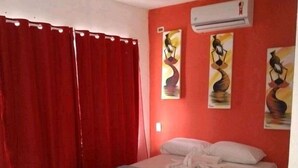 A bedroom with a bed, red curtains, and three wall-mounted paintings. - Encantos dos Sonhos (Ipojuca)
