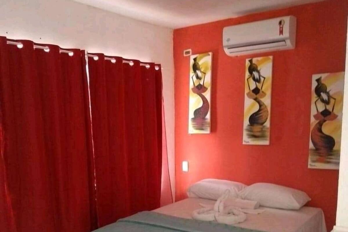 A bedroom with a bed, red curtains, and three wall-mounted paintings.