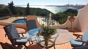 Eine Terrasse mit einem Glastisch, Stühlen und Blick auf das Meer und die Stadt.