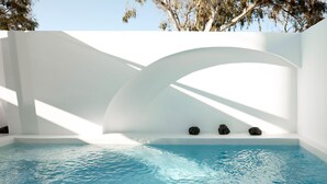 Une piscine intérieure paisible, avec une eau d’un bleu limpide, entourée de murs blancs et dotée d’une grande fenêtre en arc de cercle qui laisse entrer la lumière naturelle.