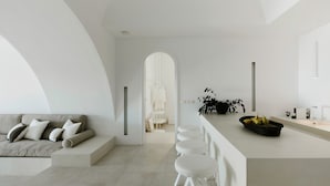 Un intérieur moderne avec un canapé, des tabourets de bar blancs, un saladier de fruits et un design minimaliste.