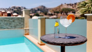 A cocktail glass with ice and an orange slice on a round table by a pool. A bottle of liquor is also on the table. - Cotobro Rental House (Almuñécar)