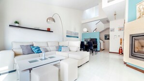 A modern living room with a white sofa, a coffee table, and a dining area with a blue accent wall. - Cotobro Rental House (Almuñécar)