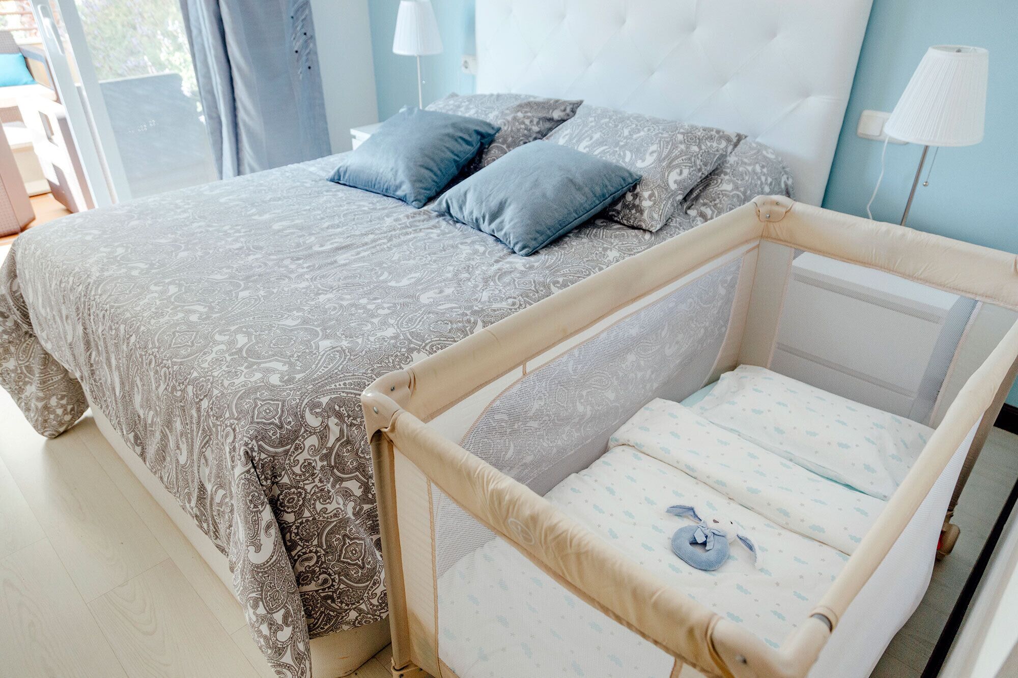 A bedroom with a large bed, a baby crib, and a window with curtains.
