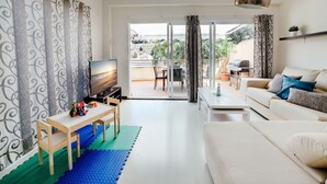 A modern living room with a TV, a sofa, a coffee table, and a balcony with outdoor furniture. - Cotobro Rental House (Almuñécar)