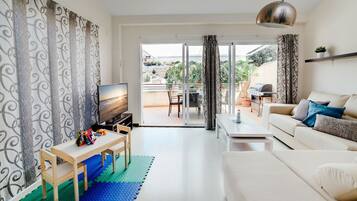 Un salon moderne avec un téléviseur, un canapé, une table basse et un balcon aménagé avec du mobilier d’extérieur.