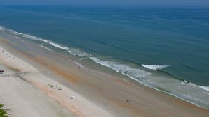 Une vaste plage offrant une vue dégagée sur l’océan, un rivage sablonneux et quelques parasols.