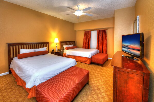 A hotel room with two beds, a TV, a desk, and a ceiling fan.