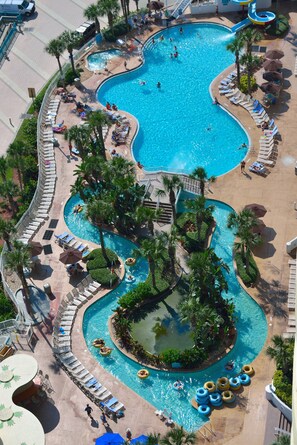 A large, winding pool with multiple sections, surrounded by palm trees and lounge chairs.