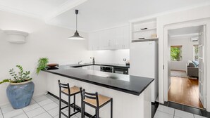 A modern kitchen with white cabinetry, a black countertop, and a large island with bar stools. - 74 Alamanda Palm Cove (Palm Cove)