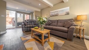 A living room with a sofa, a coffee table, and a lamp. There is a painting on the wall and a window with a view of the outside. - Sandpiper's Cottage, South Creake, Norfolk (South Creake)