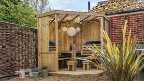 A wooden outdoor seating area with a pergola, cushions, and potted plants. - Sandpiper's Cottage, South Creake, Norfolk (South Creake)