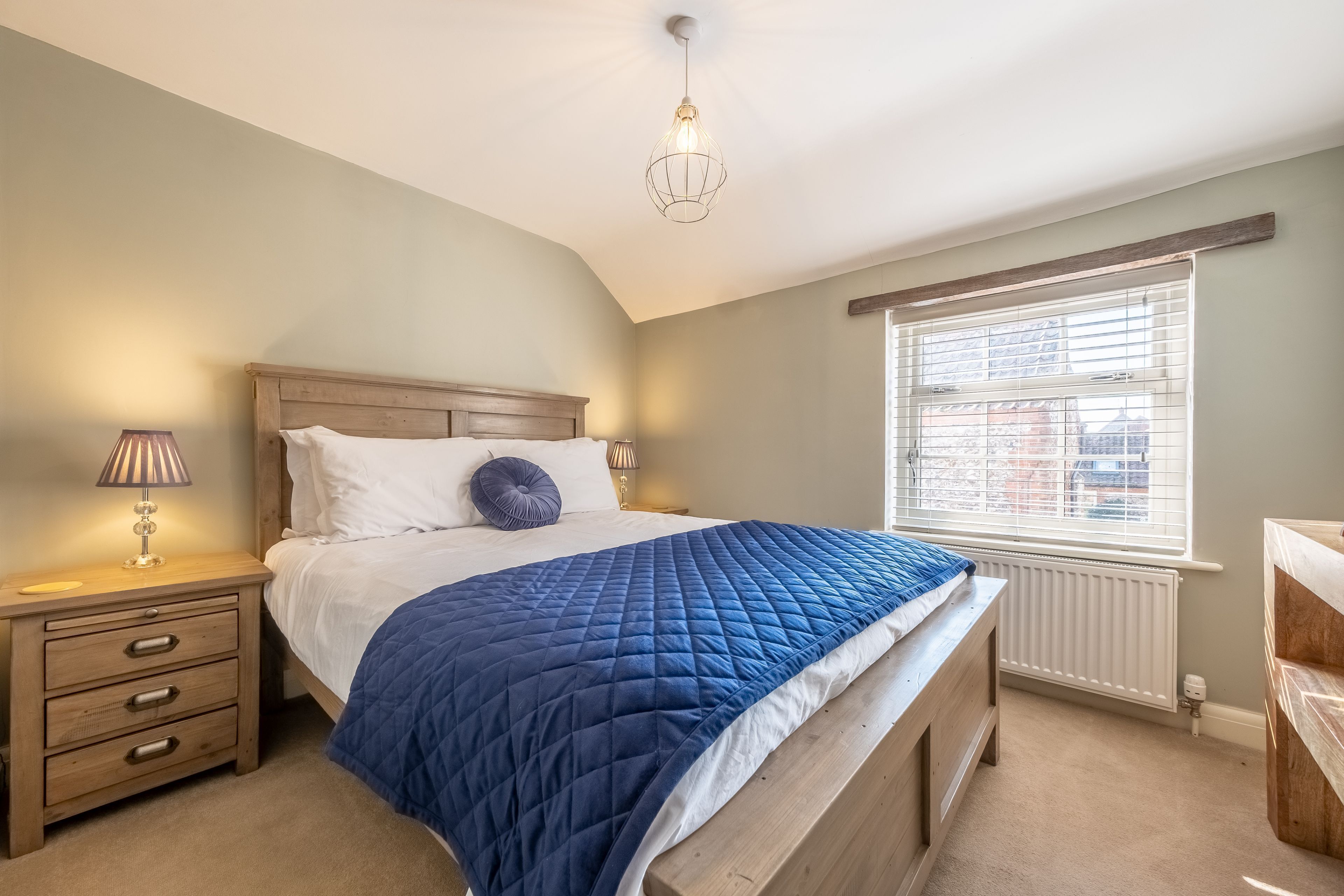 A bedroom with a bed, bedside table, lamp, and window.