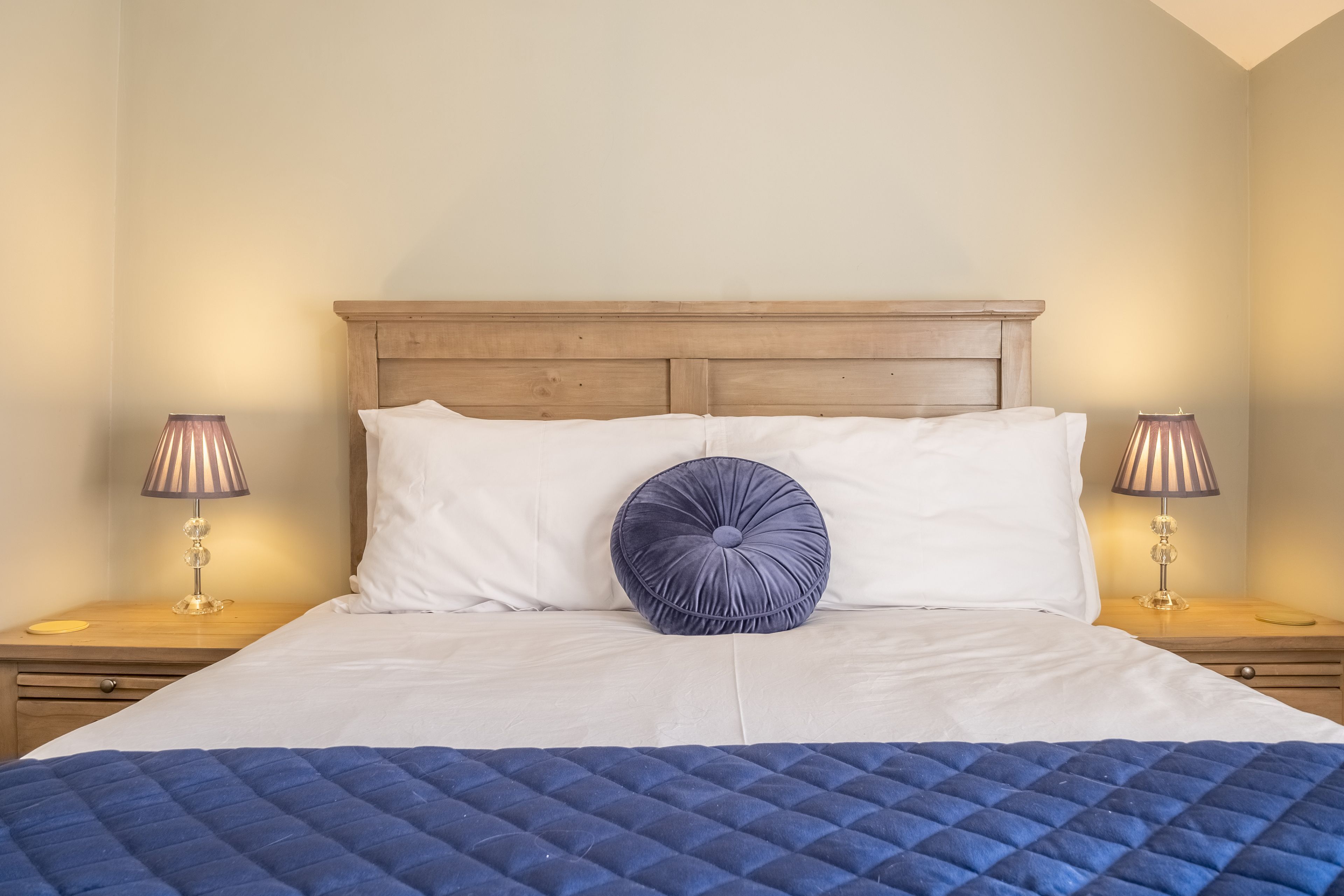A neatly made bed with a blue quilt, a wooden headboard, and two bedside lamps.