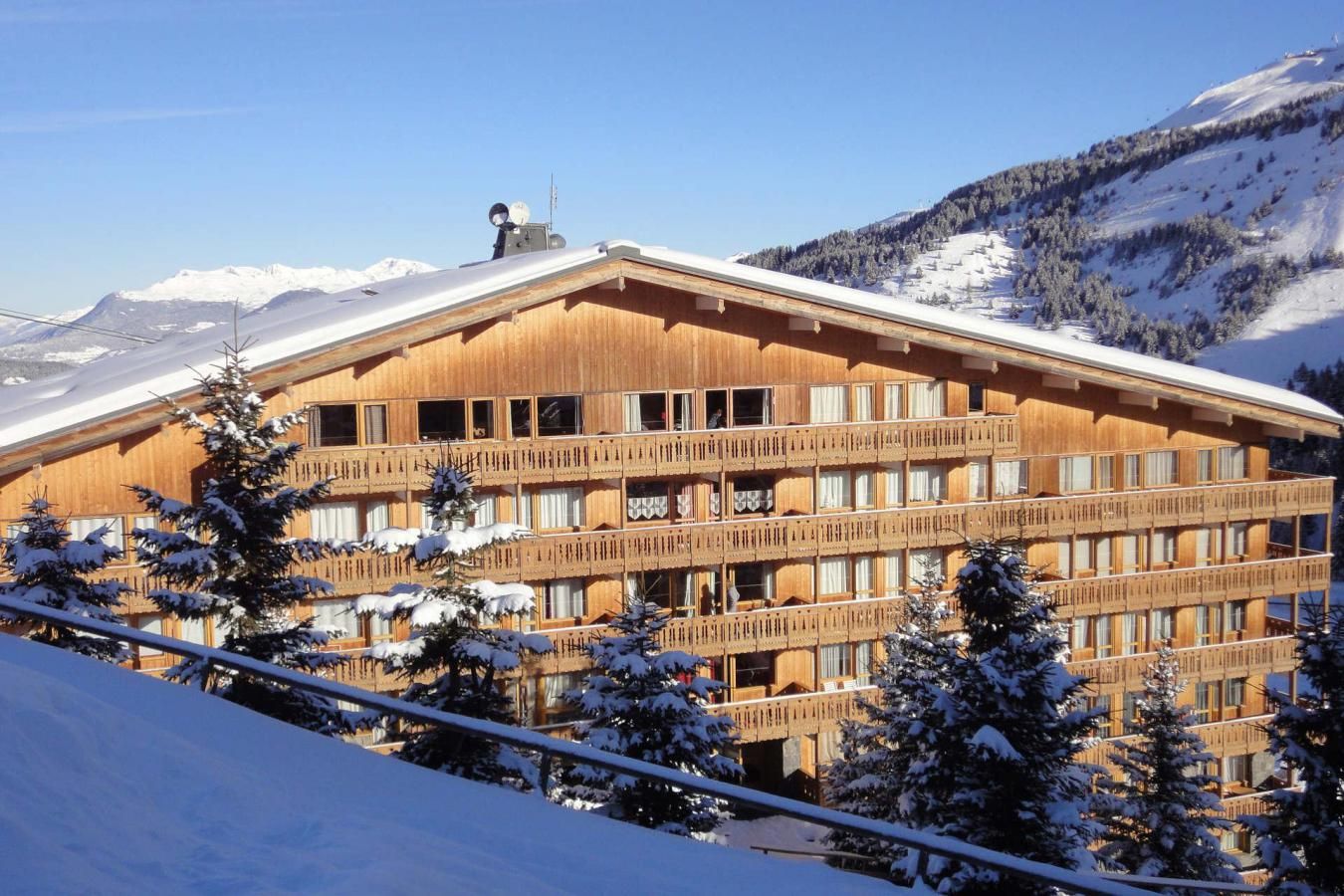 Ein mehrstöckiges Holzgebäude mit Balkonen, umgeben von schneebedeckten Bäumen und Bergen.
