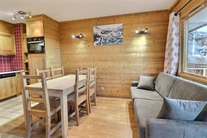 A wooden interior with a dining table, chairs, a sofa, and a kitchen area.