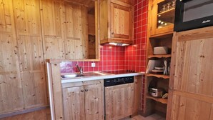 Una cocina compacta con armarios de madera, lavavajillas integrado y salpicadero de baldosas rojas.