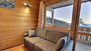 Un interior de madera con un sofá y un amplio ventanal con vistas a un paisaje montañoso.