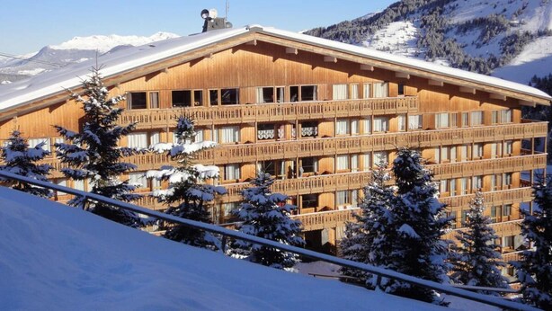 Un edificio de madera de varios pisos con balcones, rodeado de árboles nevados y montañas.
