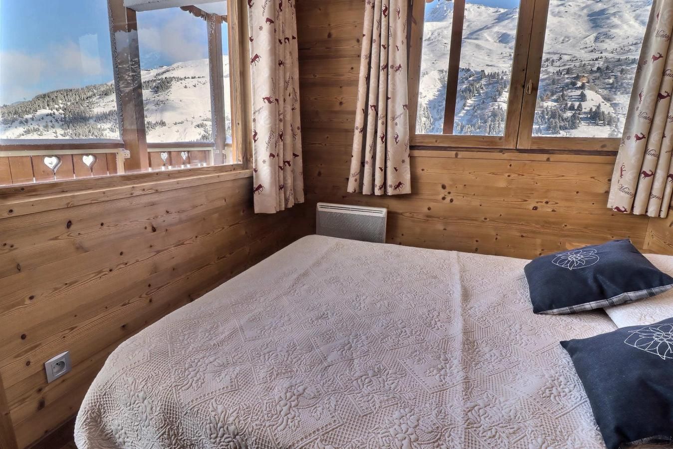A wooden room with a bed, curtains, and a window with a snowy mountain view.