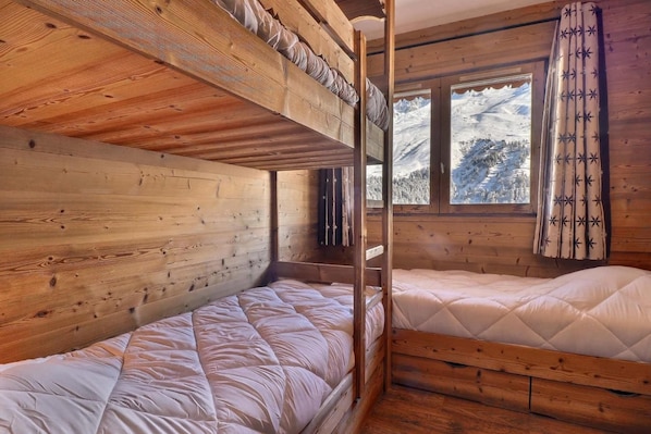 A wooden cabin room with bunk beds and a window with a view of a snowy landscape.