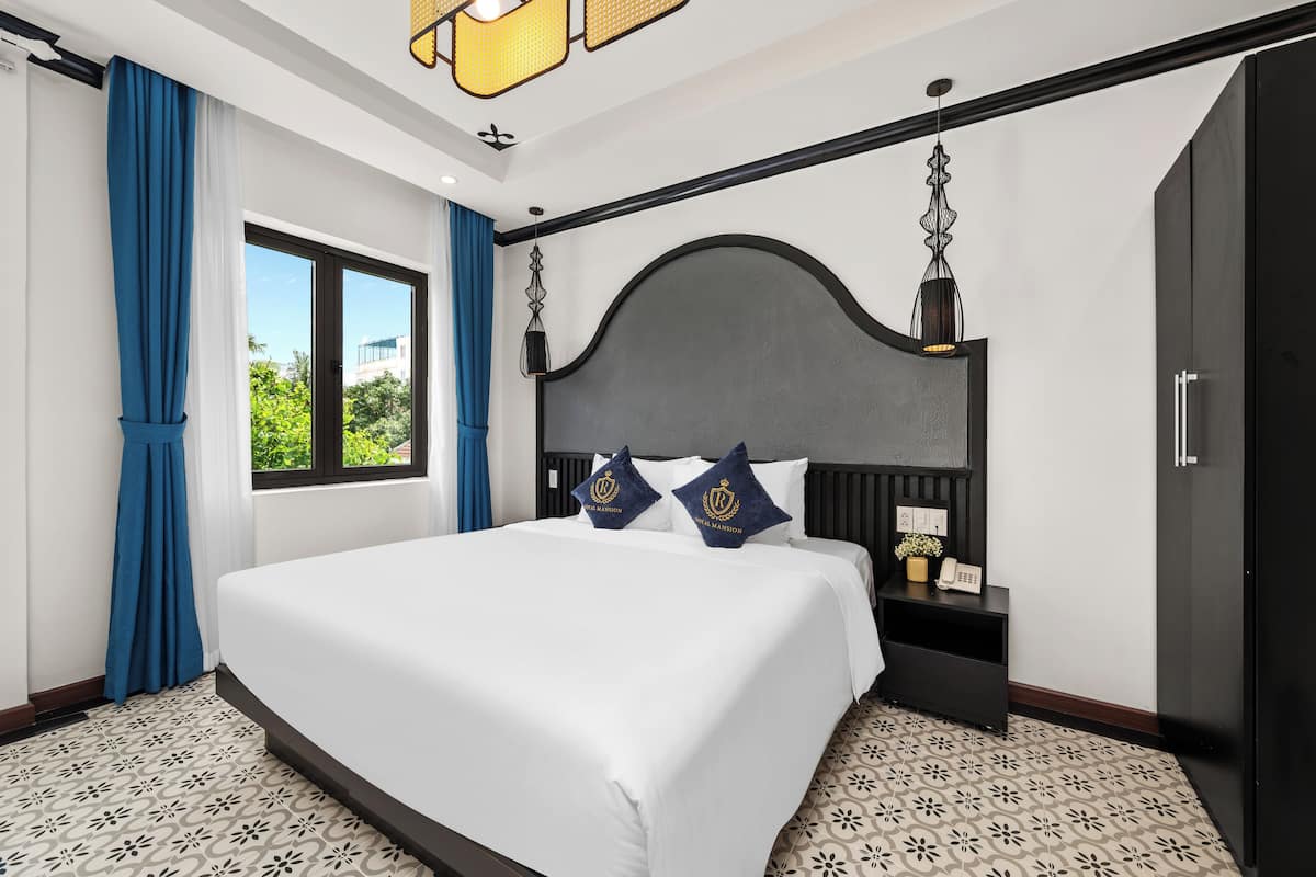 A hotel room with a large bed, a nightstand, a wardrobe, and a window with curtains.
