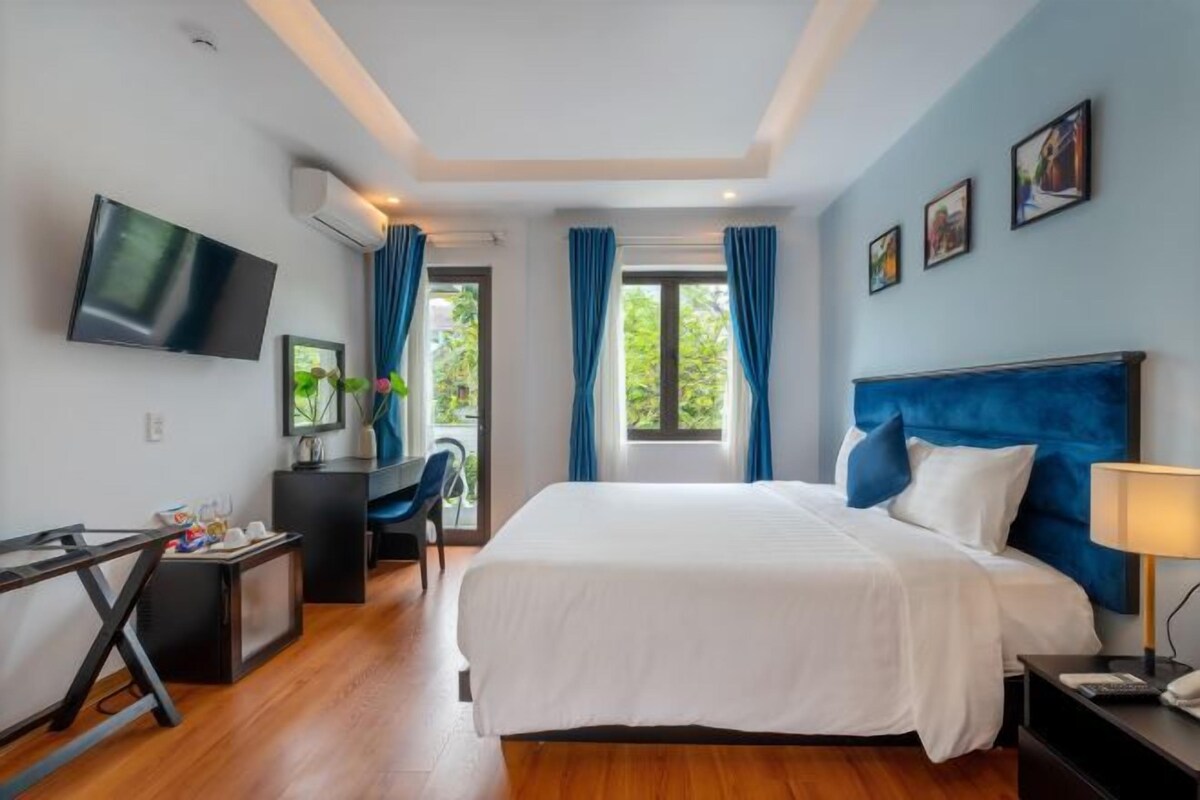 A modern hotel room with a large bed, a desk with a chair, a flat-screen TV, and a window with curtains.