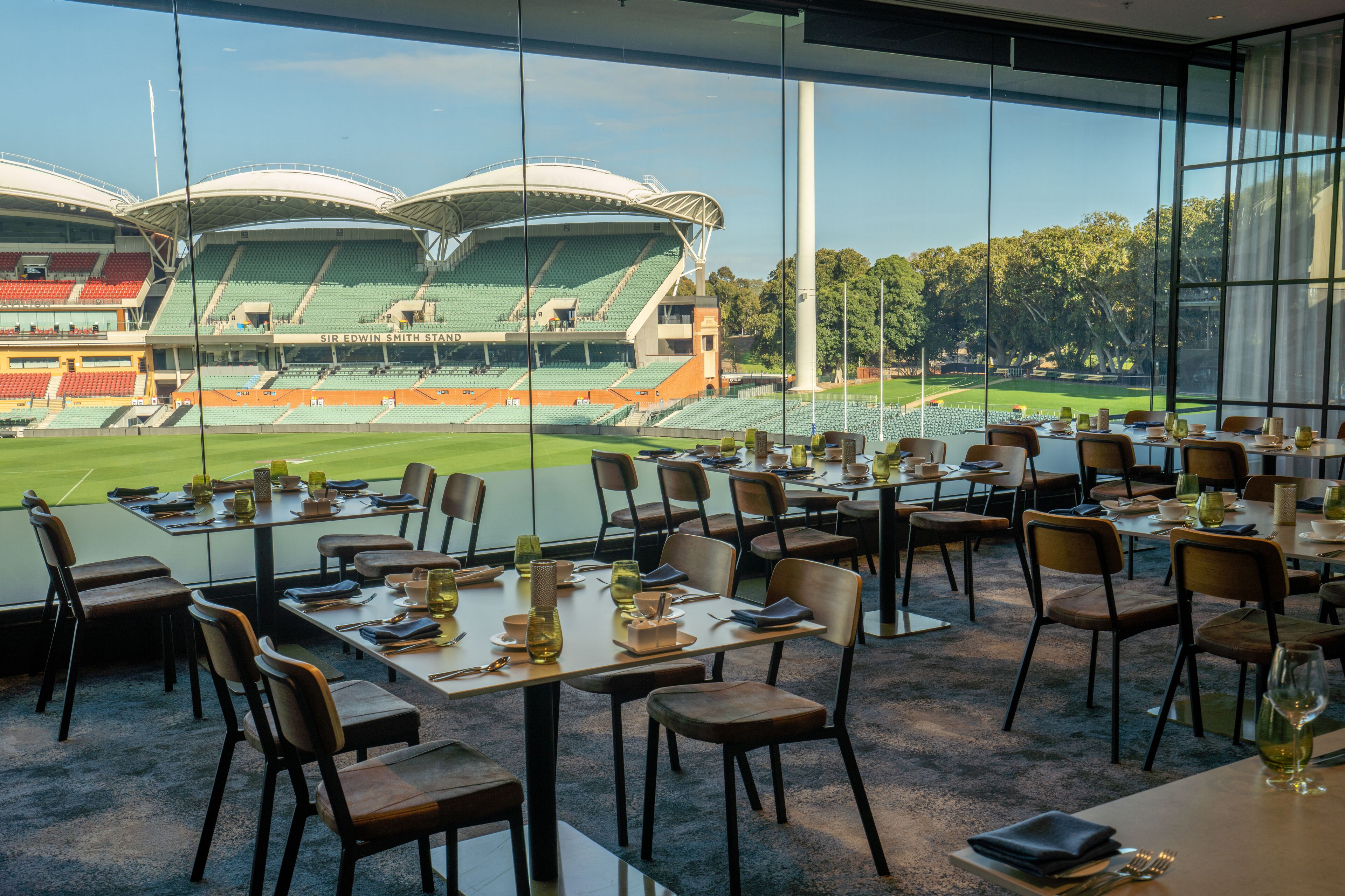 Un restaurante con mesas dispuestas para comer, grandes ventanales que ofrecen vistas a un estadio.