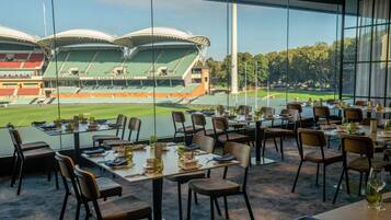 Un restaurante con mesas dispuestas para comer, grandes ventanales que ofrecen vistas a un estadio.