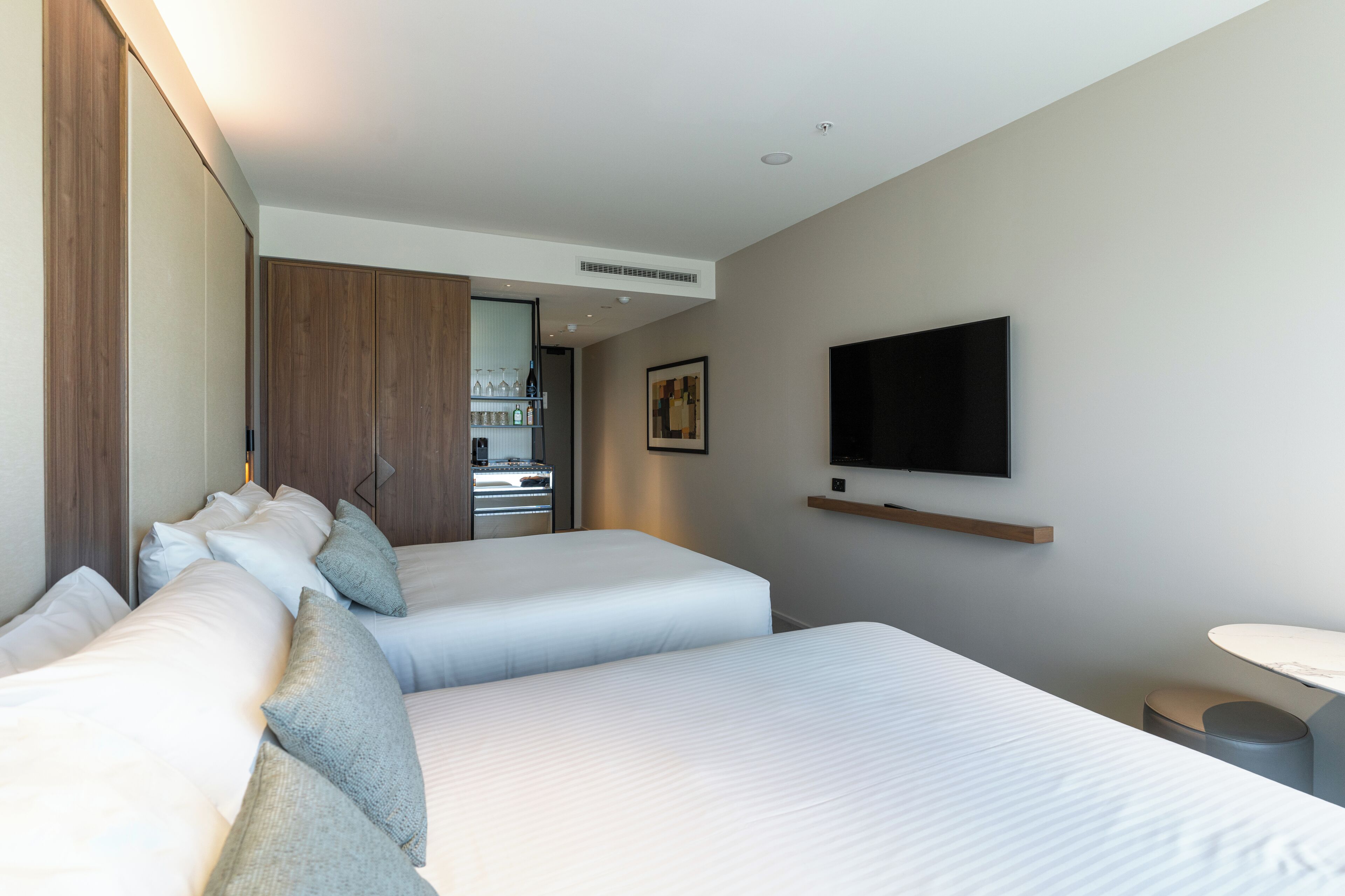 A hotel room with two beds, a TV mounted on the wall, a small table, and a minibar.