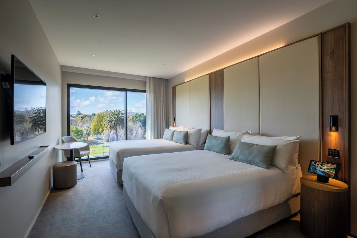 Une chambre d’hôtel moderne équipée de deux lits, d’une télévision, d’un bureau et offrant une vue sur l’extérieur.
