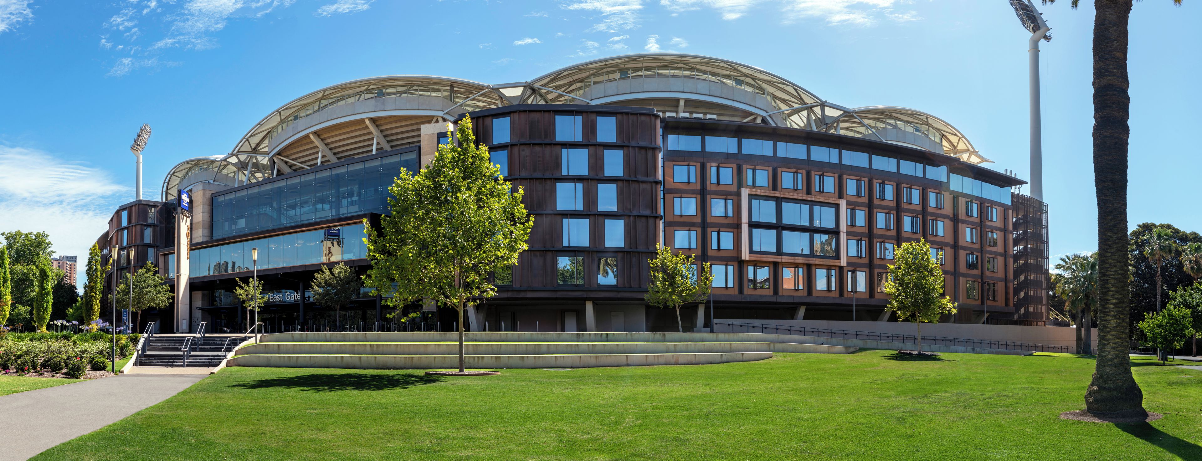 Een modern gebouw met een golvende gevel, grote ramen en een centrale binnenplaats met trappen die leiden naar een uitkijkpunt.