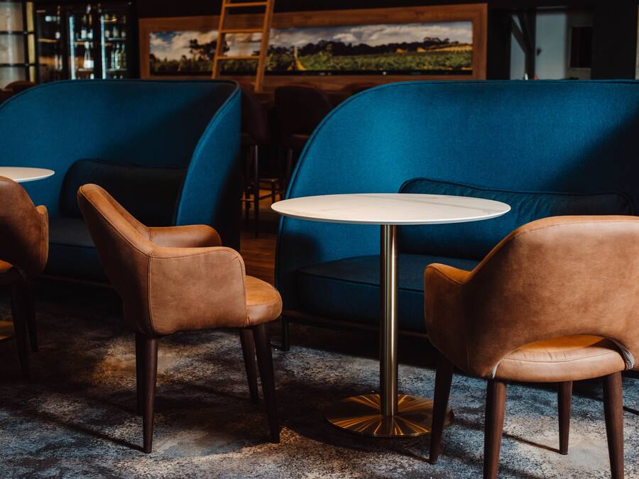Un área de descanso con sofás tapizados en azul y sillones de cuero marrón, una mesa redonda y suelo de madera.
