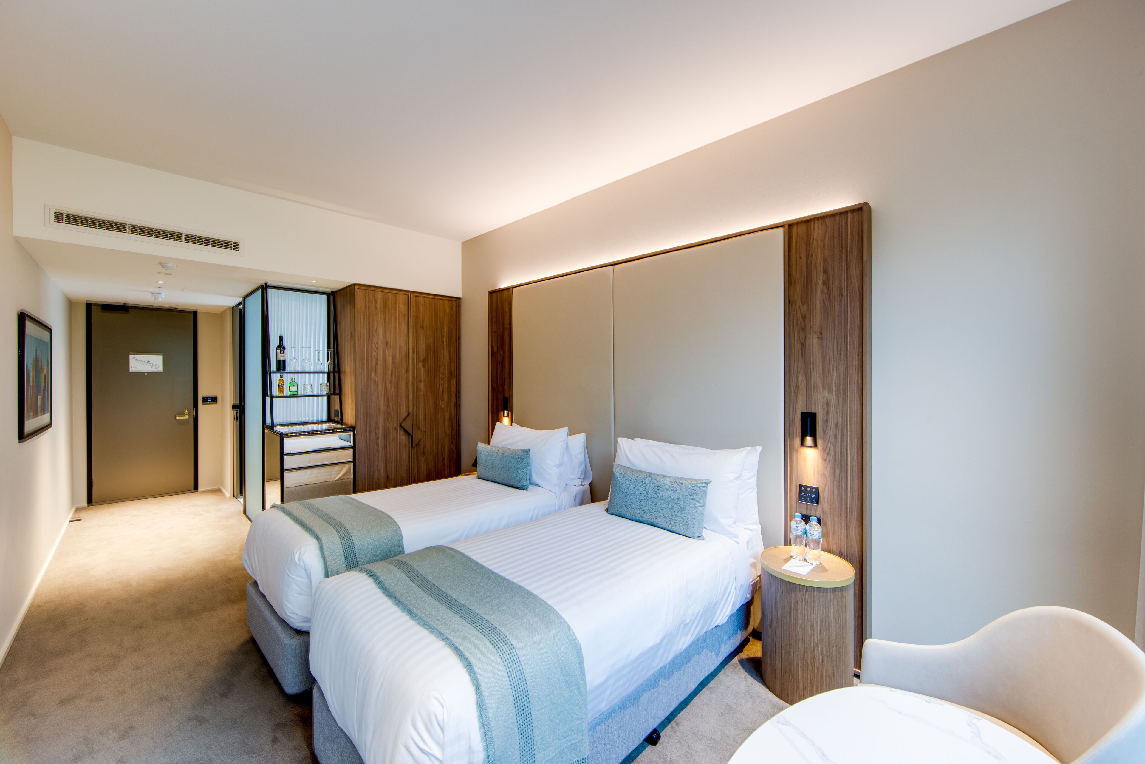 Et hotelværelse med to senge, et siddeområde, et lille bord med lampe og et spejl.
