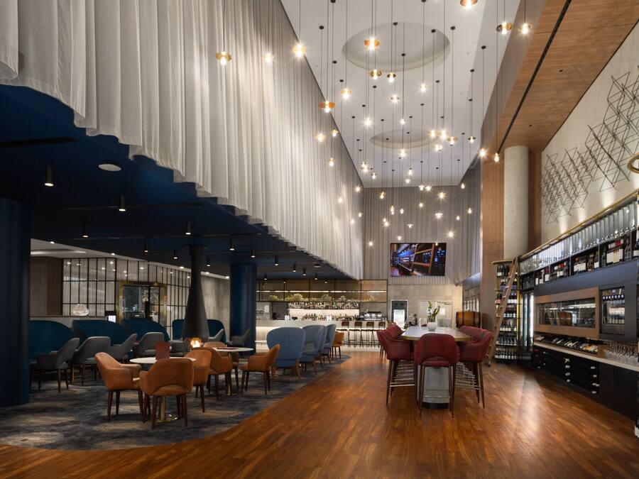 A spacious bar area with wooden flooring, multiple seating arrangements, and a variety of wine bottles on shelves.